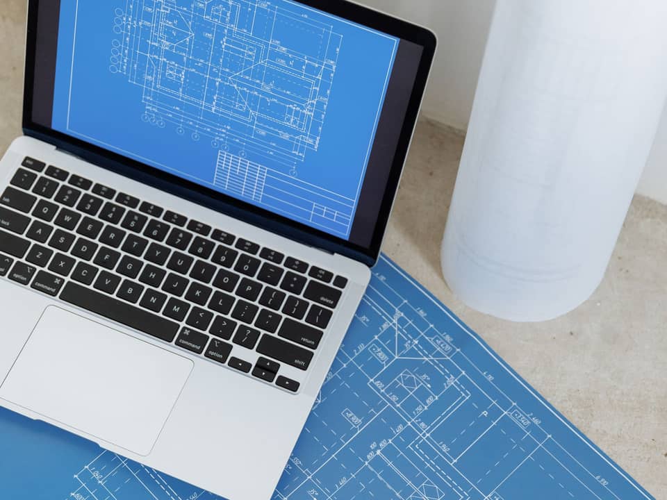Site plan blueprints and a laptop on a desk